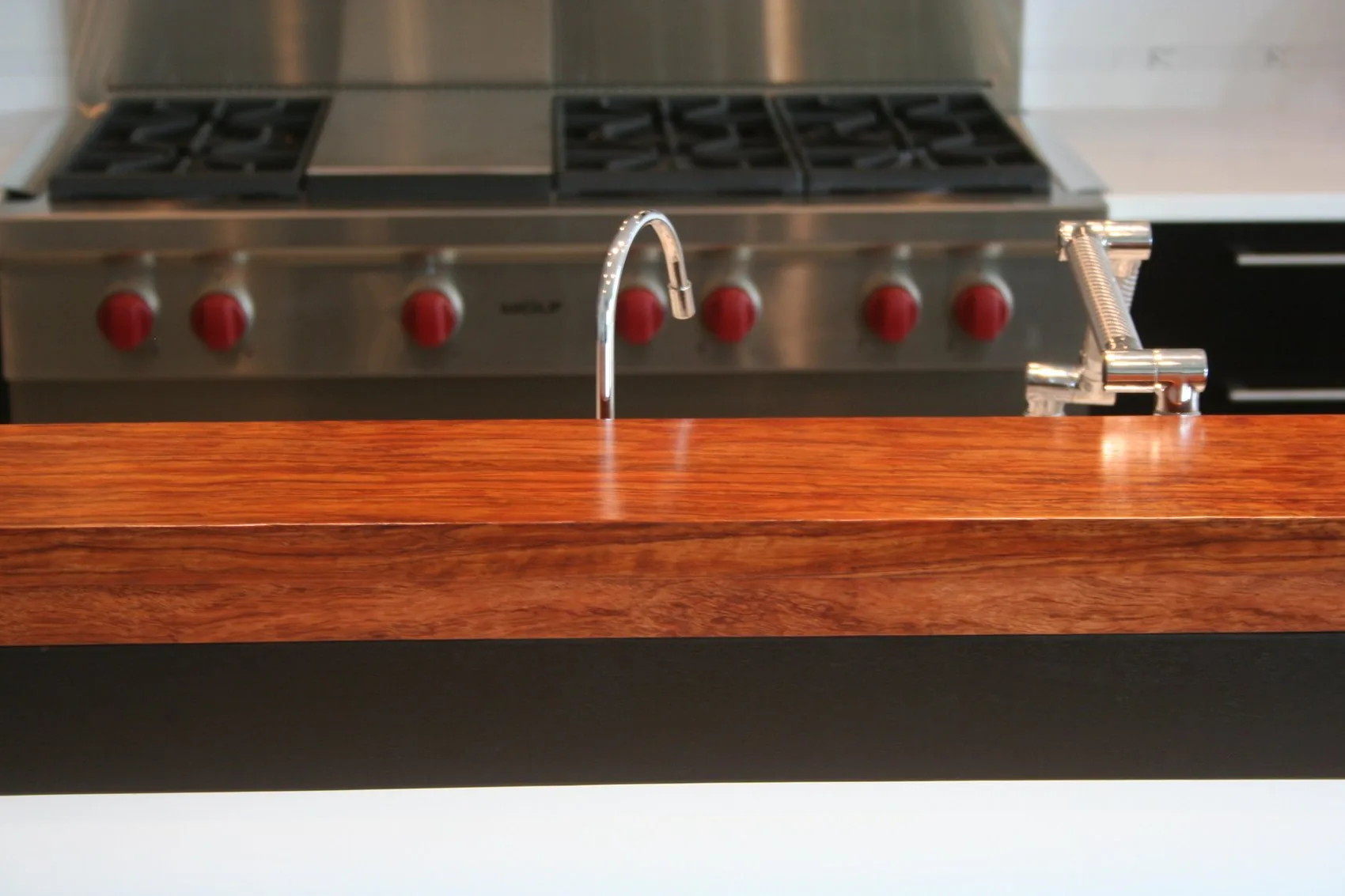 A Bubinga hardwood wall cap running across a kitchen island in front of a stainless range.