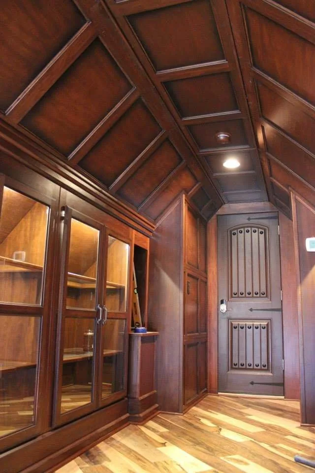 An arched wooden door with iron hardware at the end of the paneled hallway.
