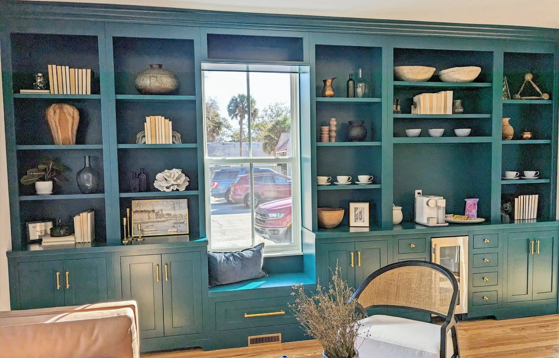 A full wall of built-in cabinetry and open shelving painted deep green, with a window seat in the middle.