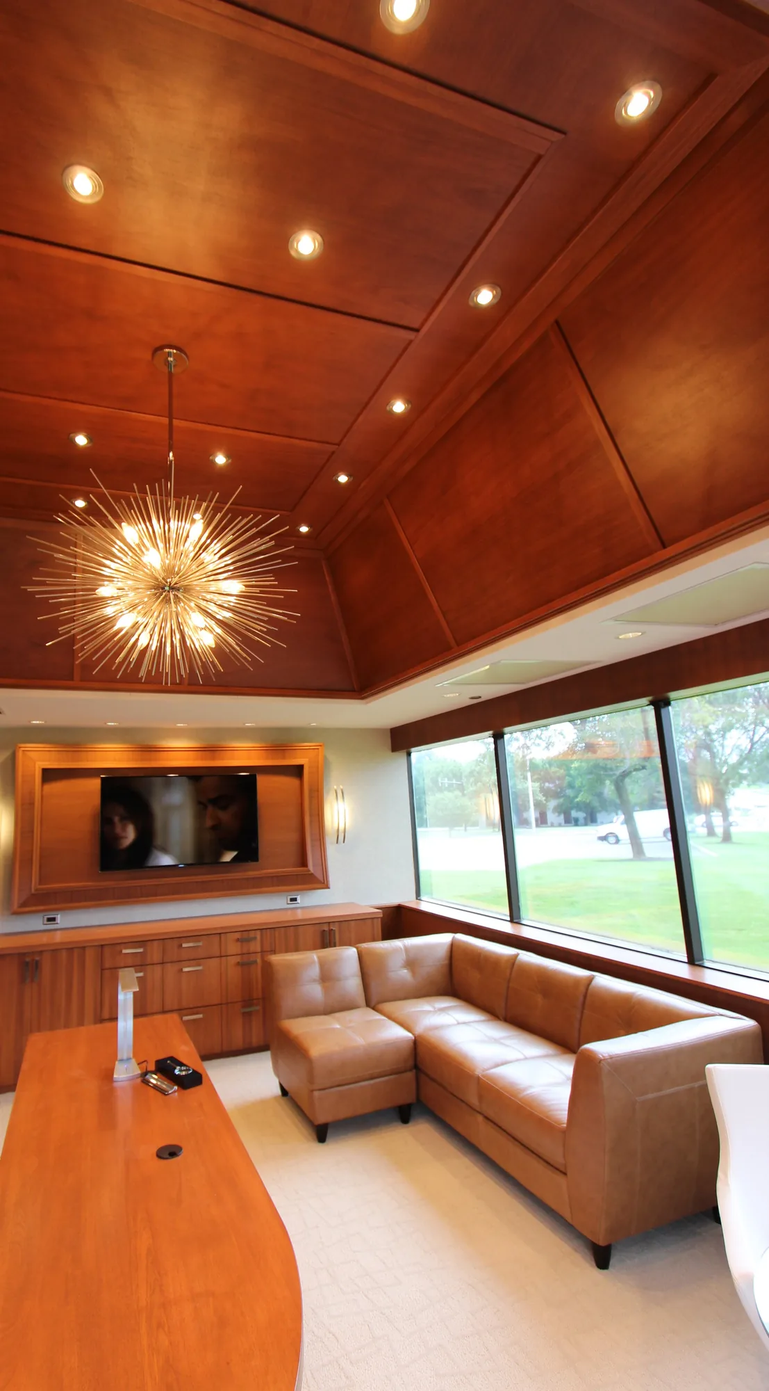 A private office with a coffered wood ceiling, a framed media wall, and a long desk.